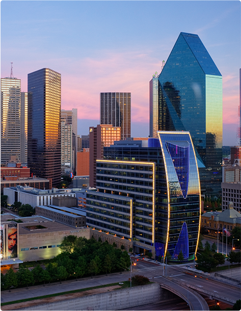 Several buildings in the Dallas city skyline reflecting the setting sun