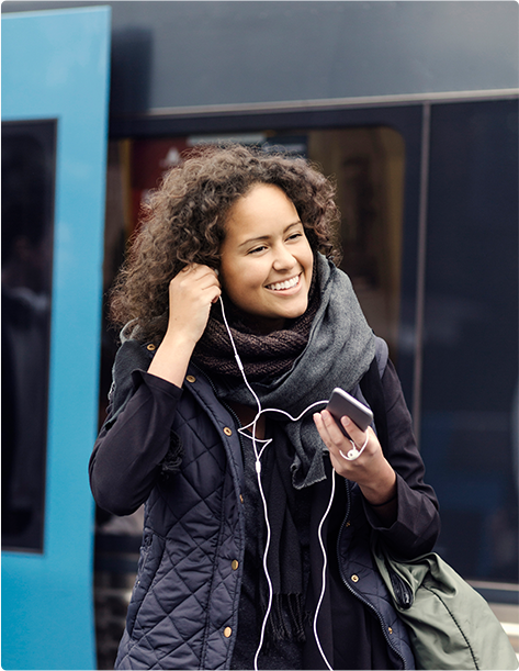 A smiling woman putting her headphones in her ears as she walks away from a commuter train