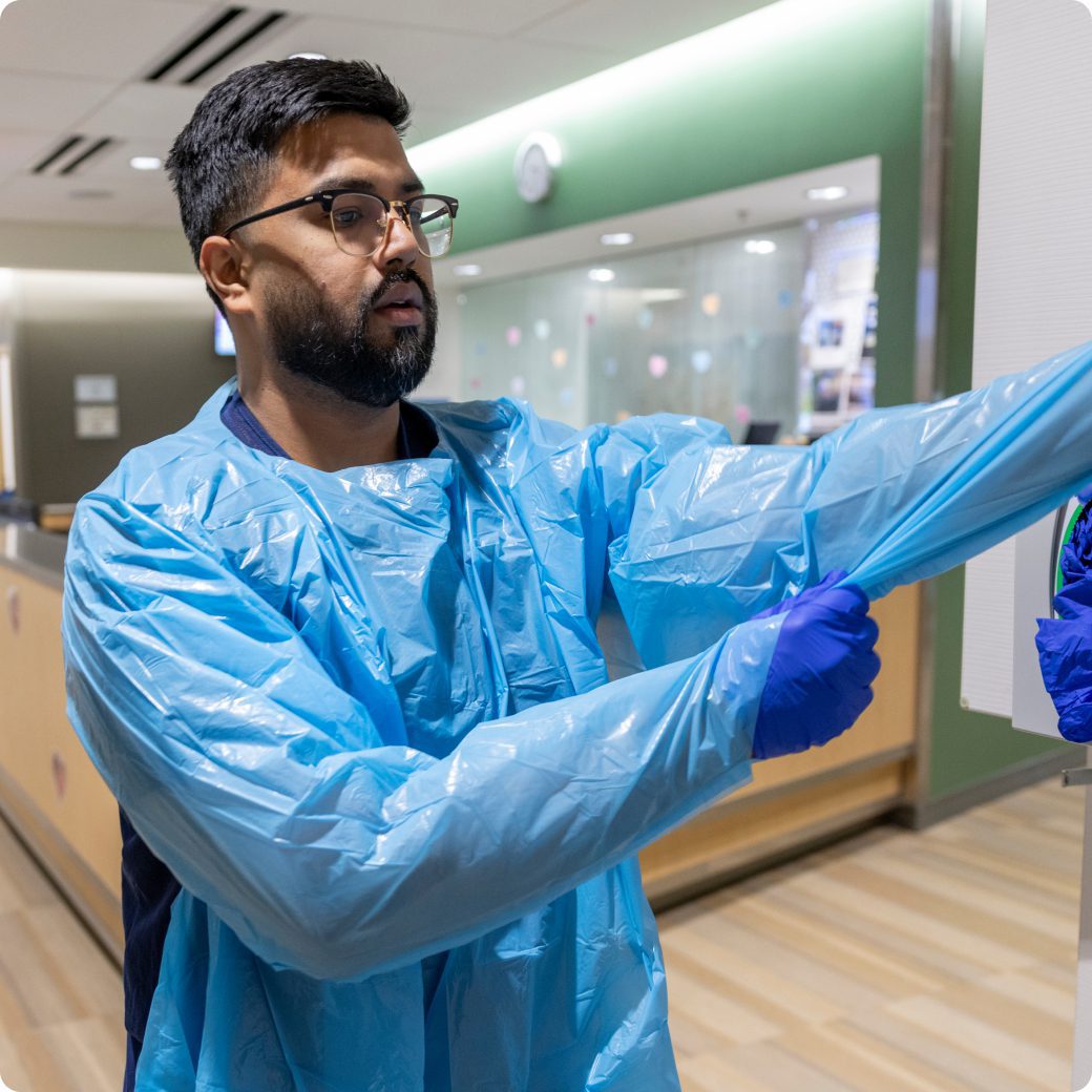 A nurse putting on a disposable blue gown and gloves in a hospital setting.