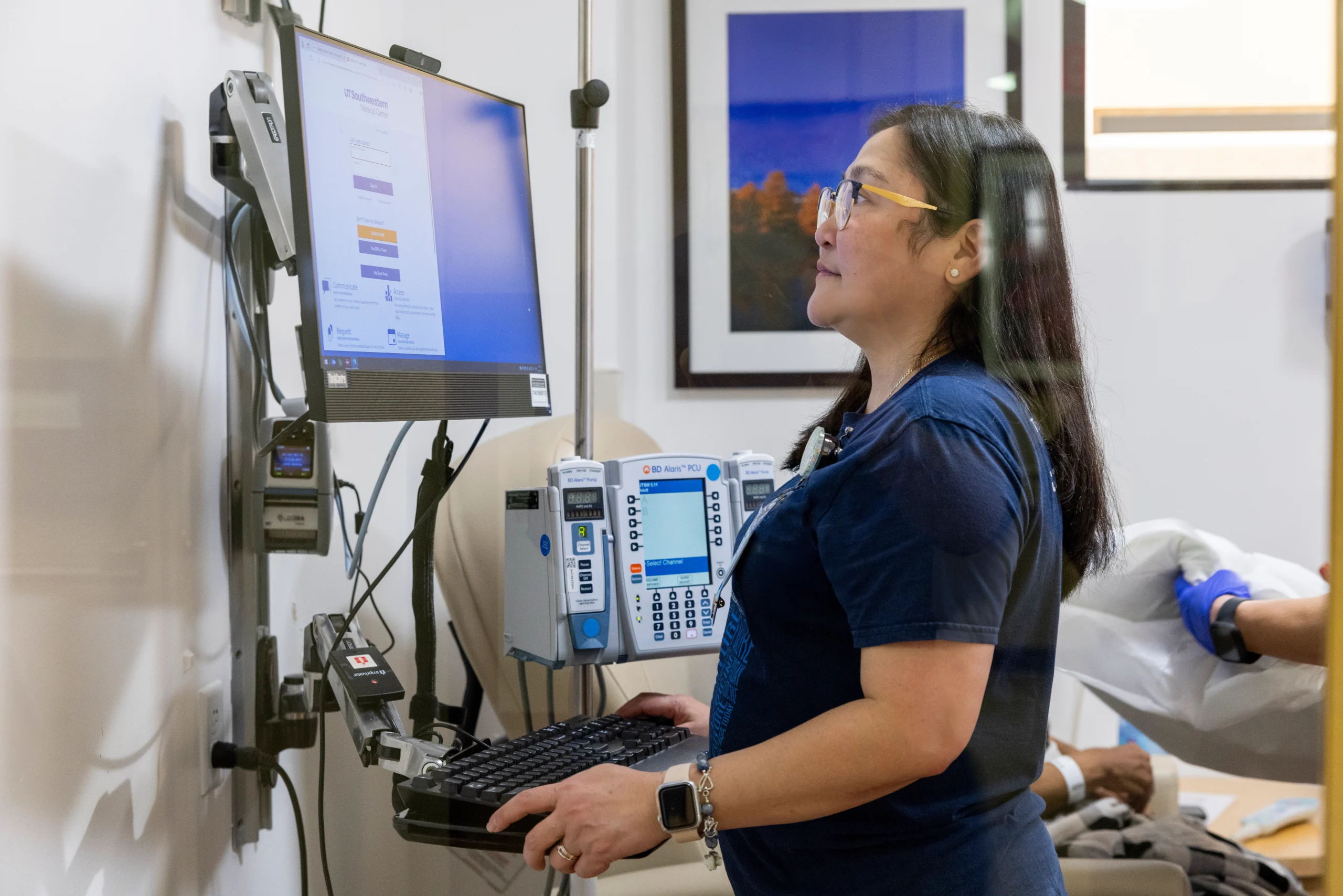  Health care professional reviewing patient information at a computer beside clinical monitoring equipment.